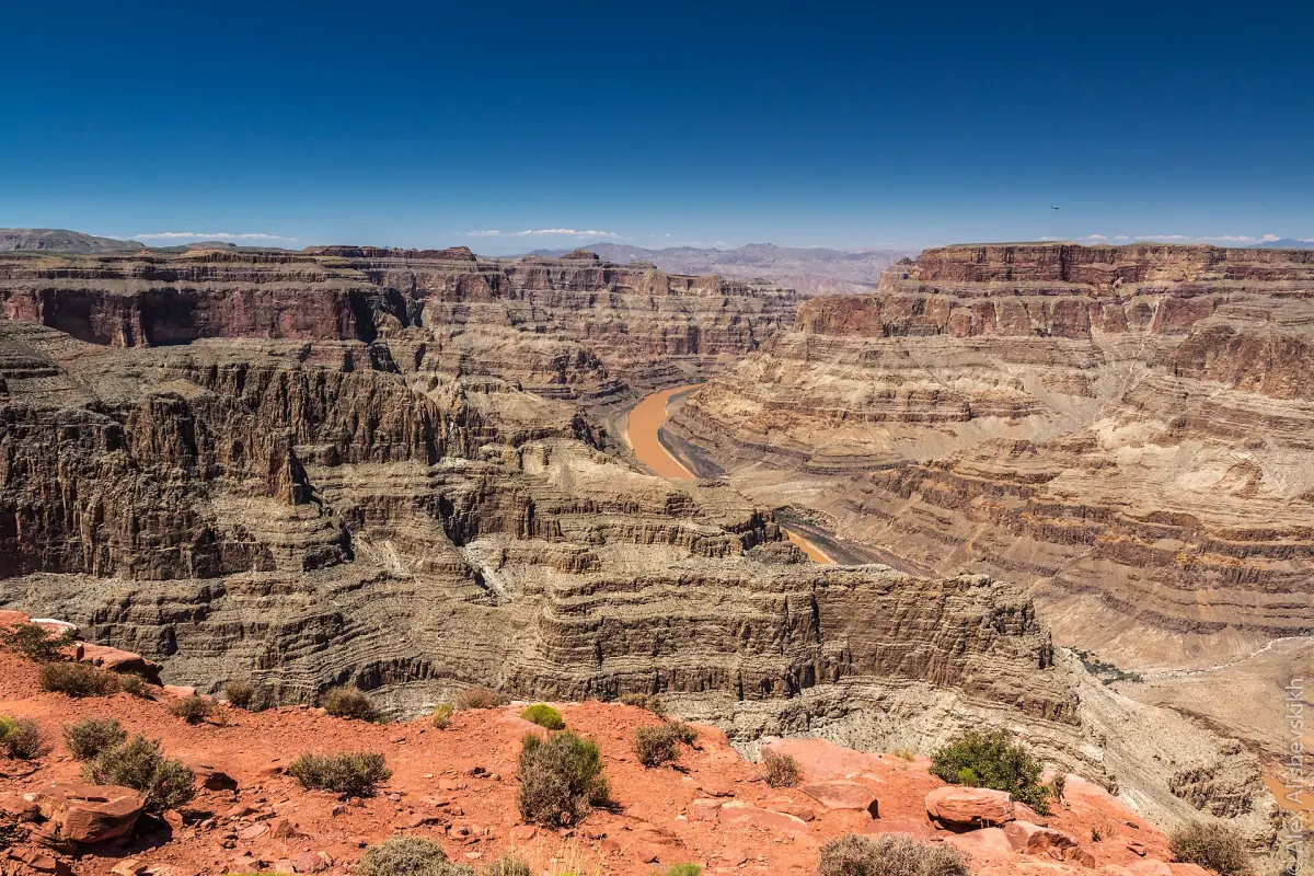 Layered red and grey canyon cliffs with the Colorado River winding far below